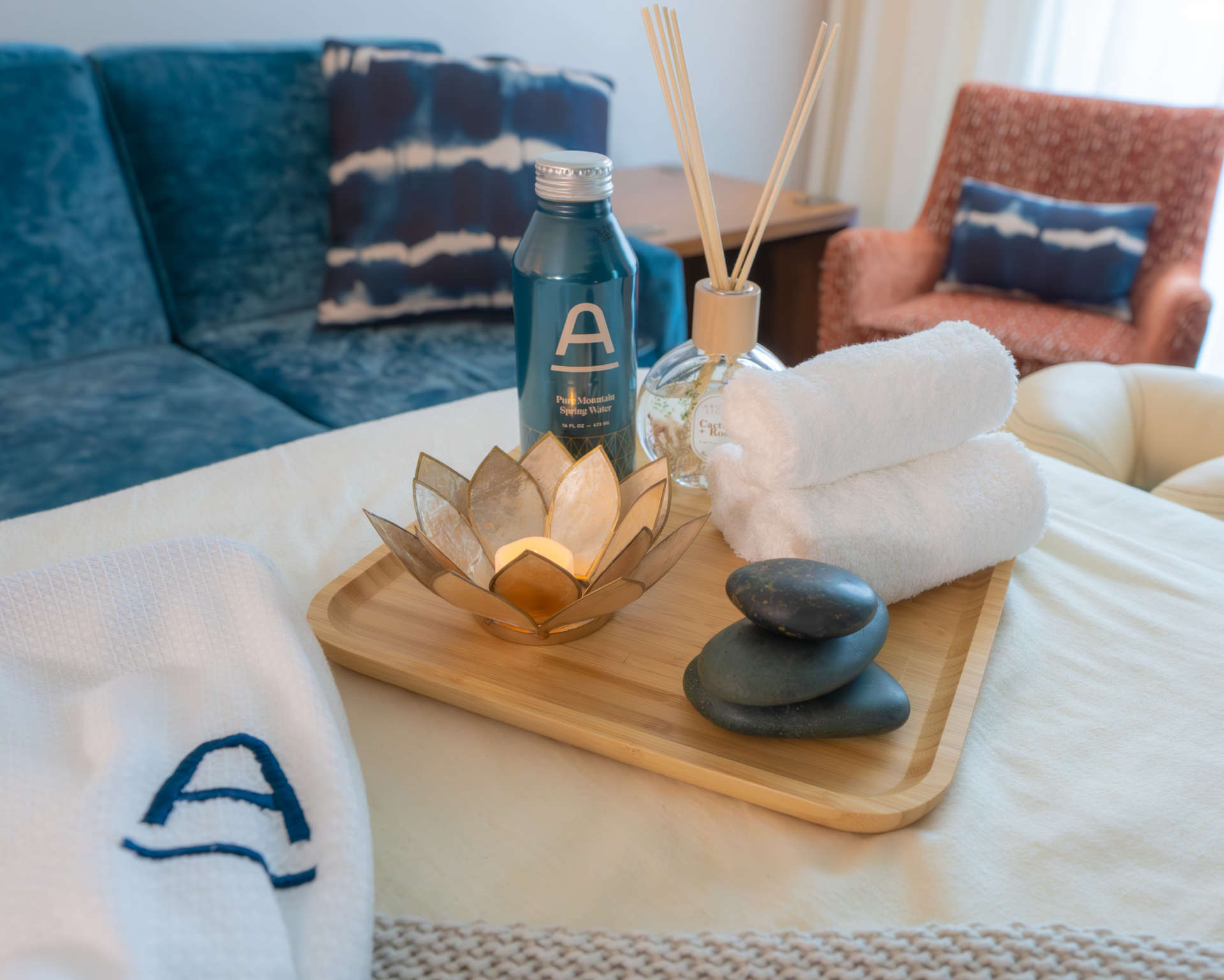 Spa items on a wooden platter at The Ameswell Hotels, including hot stones, candle, spring water, hot towels, and soothing fragrances.